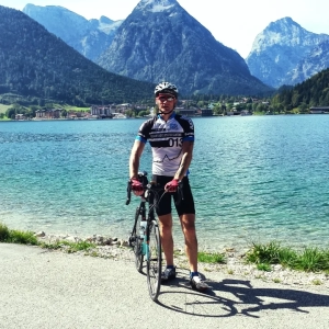 Cycling Guide, Jason Wright, standing on the shores of glacier lake, Lake Achensee, in the German Alps just before crossing the border in Austria on route to Italy.