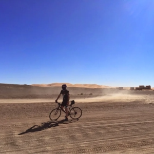 Cyclist standing in the Sahara desert avoiding a small sand funnel while cycling to the Erg Chebbi dunes, Merzouga after cycling the road to the Sahara from Marrakesh organised by cycling holiday company "European Cycling Tours"