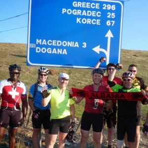 Group of cyclists standing at road sign in Albania cycling to Macedonia while on group cycling holiday organised by European Cycling Tours