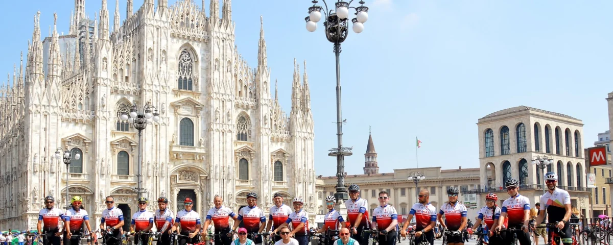 Group of cyclists celebrating the finish of a munich to milan tour at milan cathedral