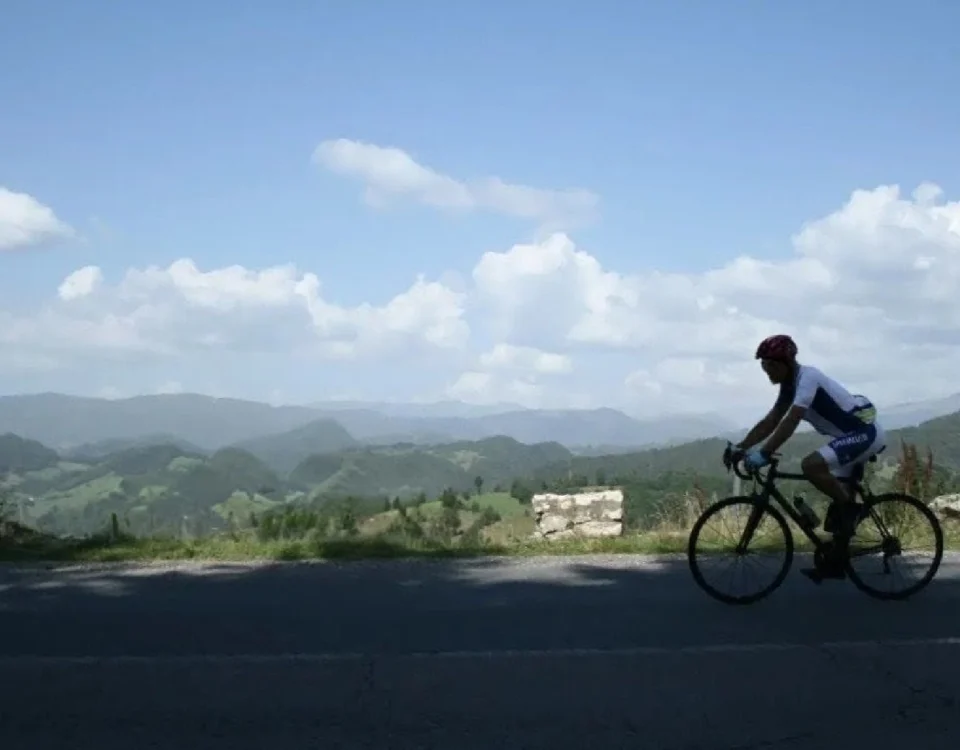 A panoramic view of a cyclist on a scenic winding road with a Transylvanian mountain backdrop; explore our detailed guide to planning a professional cycling holiday in Romania.
