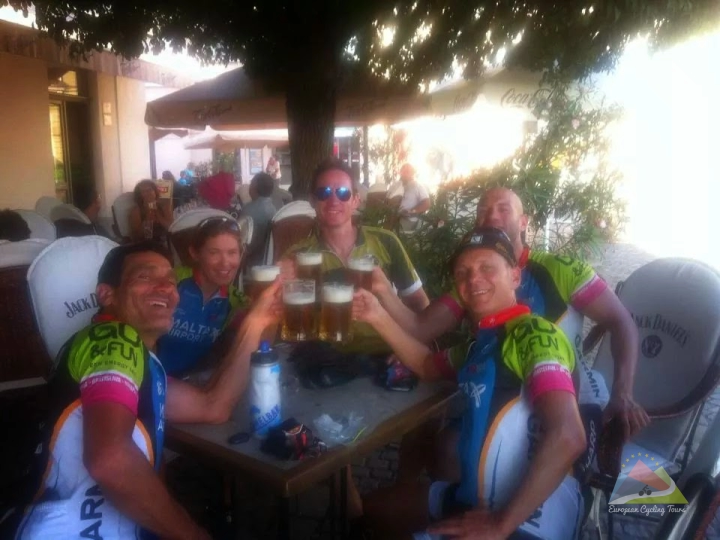 A relaxed group of riders enjoying drinks with lead guide Jason Wright following a mountain stage; discover why our guided support makes the difference.